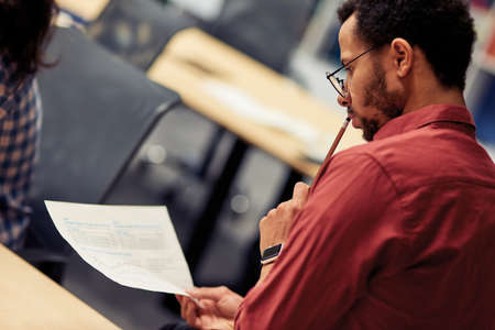 Young mixed race man analyzing document while working in the modern office, selective focus