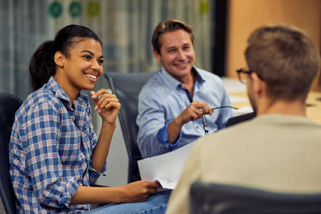Young cheerful mixed race female office worker discussing business with her colleagues while sitting...