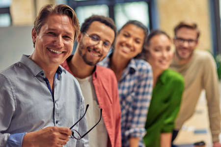 Powerful team. Group of young happy multiethnic colleagues smiling at camera while standing in the modern office, business people working togetherの写真素材