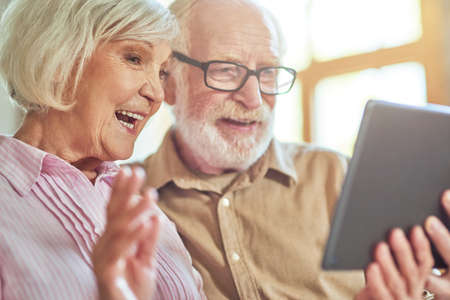 Smiling elder woman waving during video call near her husband