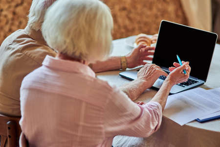 Elderly husband and wife using computer at homeの写真素材