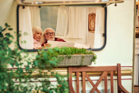 Elderly spouses lying together on the couch and holding map in their motorhomeの写真素材