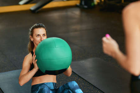 Young sportive woman in sportswear doing abs exercises exercising with fitness ball at gym with...