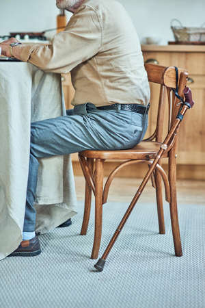 Pensioner working on laptop while sitting on wooden chair at homeの写真素材