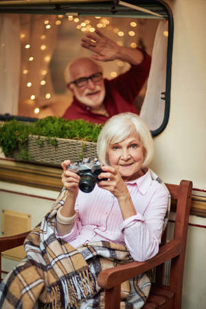 Smiling gray-haired lady sitting on wooden chair with rare cameraの写真素材