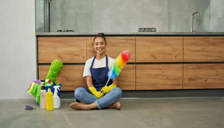 Safe and clean. Joyful young woman smiling at camera, holding cleaning duster while resting after...