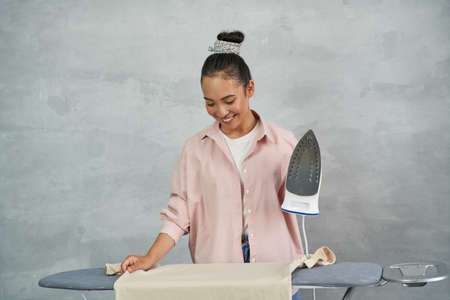 Fresh and ironed. Attractive young woman smiling while ironing clothes on ironing board at homeの写真素材