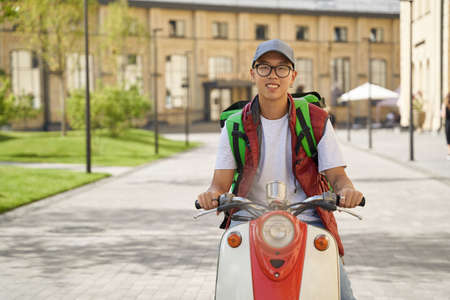 Young cheerful asian male courier with thermo bag delivering fooの写真素材