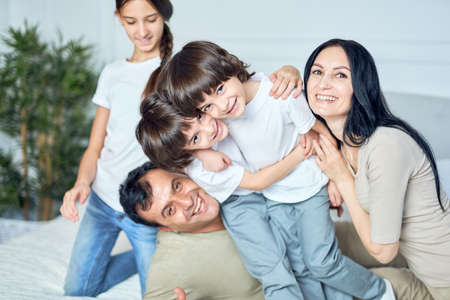 Home is where the family is. Close up portrait of happy latin family, parents and children smiling at camera while gaving fun together at homeの写真素材