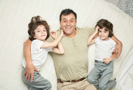 Two cute little latin boys, children and their father smiling at camera while lying together on a...