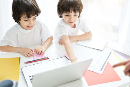 Two adorable latin boys, brothers looking focused, sitting together at the table, looking at the...