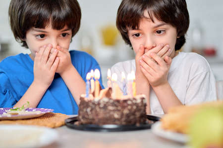 Magic moment. Adorable little hispanic boys looking at birthday cake, making wishes while getting...