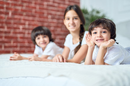 Portrait of cute little latin boy smiling at camera. Brother spending time with his siblings, lying on the bed at homeの写真素材