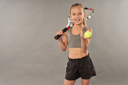 Cute little girl with tennis racket and ball on grey background. Space for textの写真素材