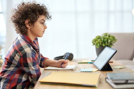 Get an education. Enthusiastic latin school boy wearing glasses making notes, having online lesson...