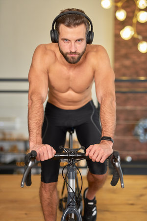 Athletic young man in headphones riding stationery bicycleの写真素材