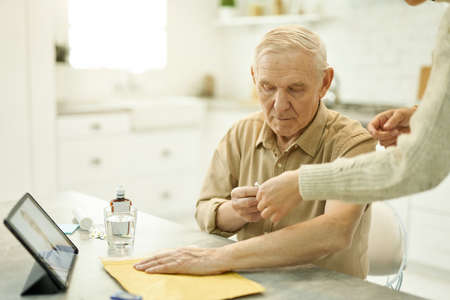 Senior man staying home and getting help with injection