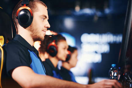 Participating in eSport tournament. Side view of fully concentrated caucasian guy, male cybersport...