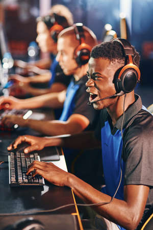 Enjoyment. Side view of a young excited african guy, male cybersport gamer wearing headphones...