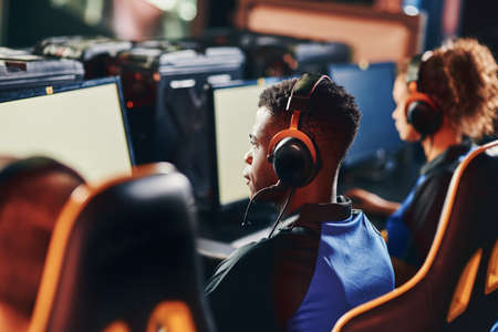 Rear view of focused young african guy, professional cybersport gamer wearing headphones playing online video games, participating in eSport tournamentの写真素材