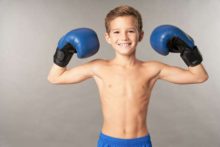 Cheerful boy in boxing gloves standing against gray backgroundの写真素材