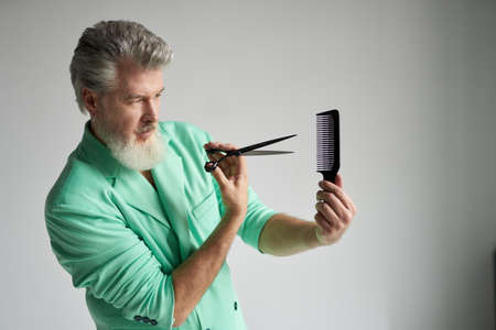 Focused gray haired mature man with beard wearing stylish outfit showing his skills while posing...