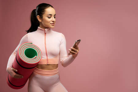 Sporty young woman with yoga mat using cellphone