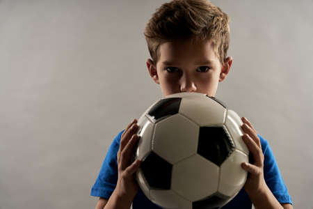 Adorable male child covering mouth with soccer ballの写真素材