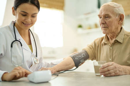Easy-going doctor using a manometer while examining her aged patientの写真素材