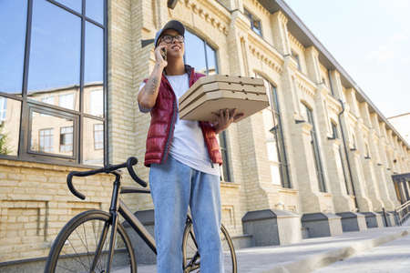 Young male courier talking by phone with customer while deliveri