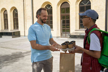 Young asian male courier with thermo bag giving four cups of cof