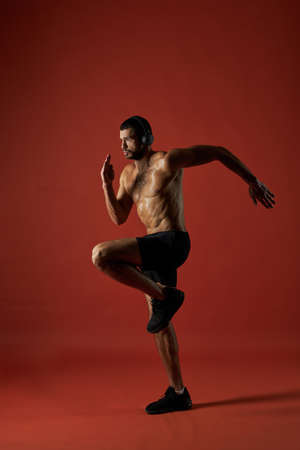 Focused athlete man in headphones doing fitness exercises isolated on red background
