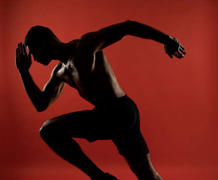 Handsome unrecognized athlete in action isolated on red background of a studioの写真素材