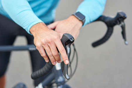 Close up shot of hands on handlebar. Professional male cyclist wearing suit standing with his bike on the road outdoorsの写真素材