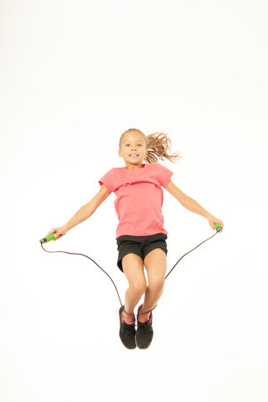 Adorable female child with skipping rope jumping in studioの写真素材