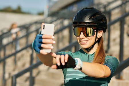 Portrait of cheerful professional female cyclist in cycling garment and protective gear smiling...