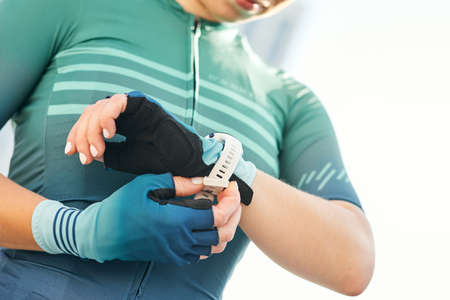 Cropped shot of professional female cyclist in sportswear putting on smart watch and cycling gloves while getting ready for trainingの写真素材
