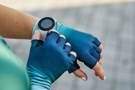 Closeup shot of hands of professional female cyclist in sportswear putting on smart watch while getting ready for trainingの写真素材