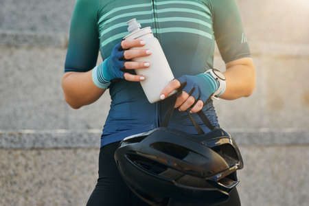 Cropped shot of young sportswoman holding black bike helmet and water bottle while getting ready for cyclingの写真素材