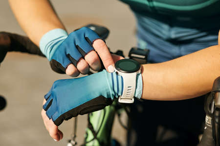 Close up shot of hands of professional female cyclist in cycling garment using smartwatch, checking results after having a training, riding bicycle on a sunny dayの写真素材