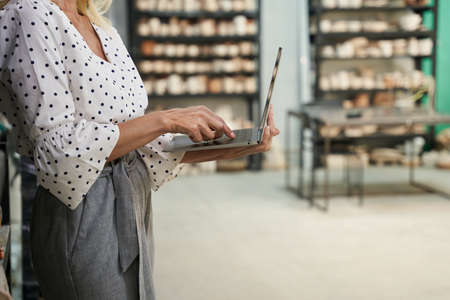 Cropped shot of female business owner typing using her laptop, standing in craft pottery shopの写真素材