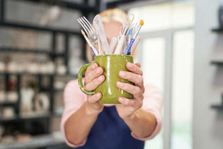 Necessary things. Close up of hands of woman holding tools, brushes for creating handmade clay...