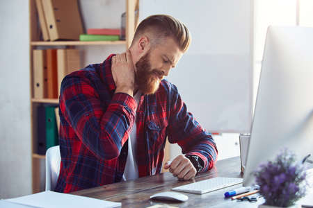 Bearded young man tired of working on pc in the office