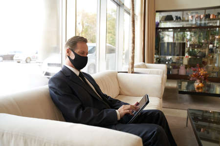 Adult hotel visitor resting with his gadget in empty hallの写真素材