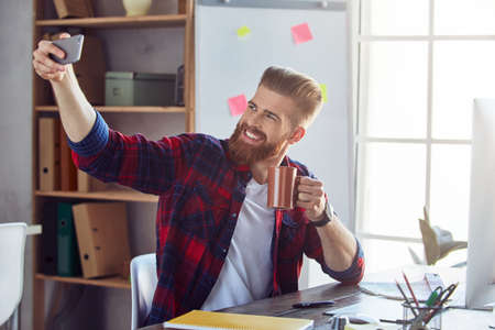 Smiling creative designer making photo on his smartphone