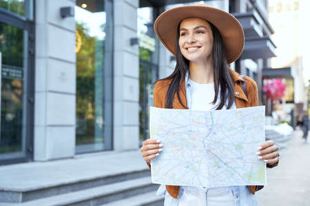 Happy attractive female in hat using map outdoorの写真素材