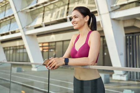 Smiling brunette in a sports top with smartphone