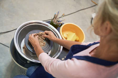 Make something unique. High angle view of woman shaping, creating handmade clay ceramics in pottery...