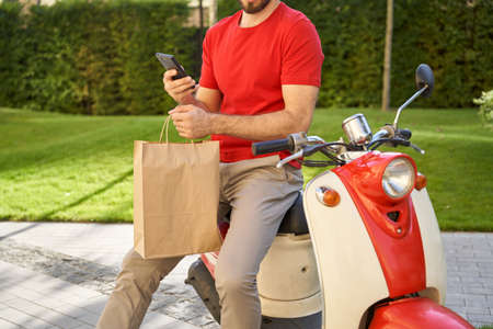 Male courier using mobile app while delivering paper eco bag witの写真素材