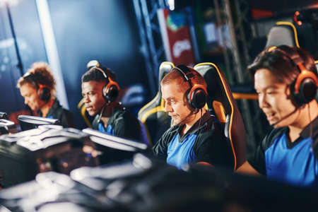 Team of four professional cybersport gamers wearing headphones participating in eSport tournament, playing online video gamesの写真素材